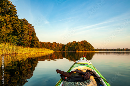 Kayak gliding across a tranquil lake, trees and reeds bathed in the golden light of the setting sun. 