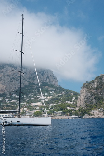 Wallpaper Mural A vibrant coastal scene in Capri, Italy, taken from the sea, with a white boat, sparkling blue waters, rugged cliffs, and the charming Mediterranean city architecture under a clear sky Torontodigital.ca