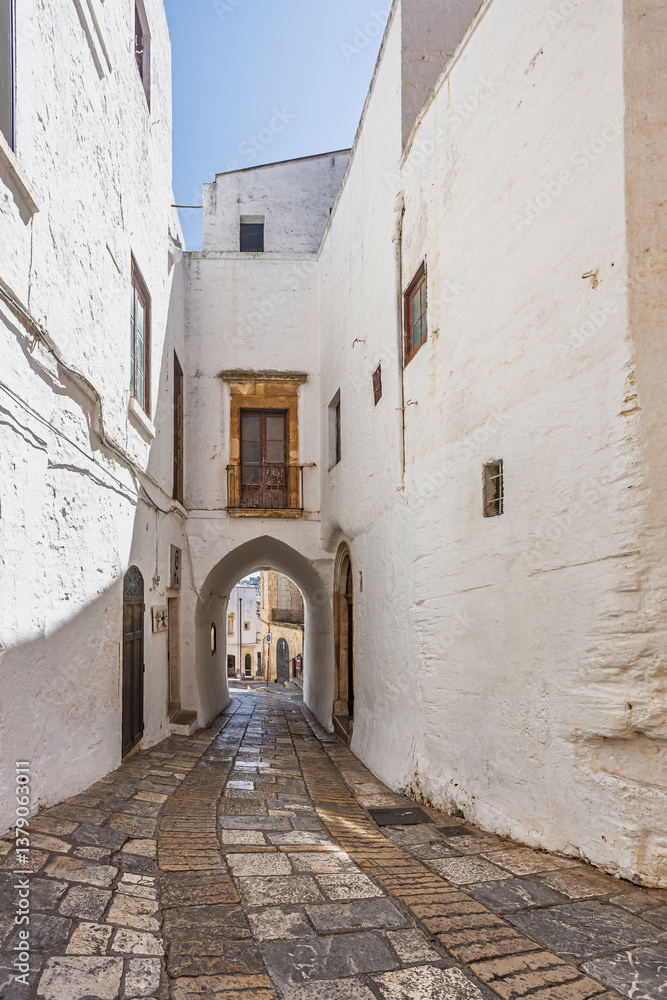Obraz premium Scenic view of Ostuni, Italy's 'White City,' showcasing whitewashed buildings under a clear blue sky, with narrow streets and historic architecture illuminated by sunlight.