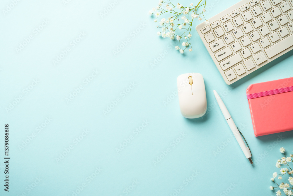 Workplace with keyboard, notebook, pen and flower on blue background.