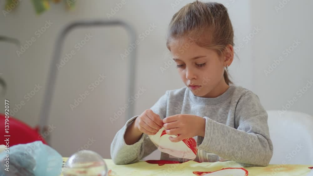 Cute girl focusing on a craft project, carefully stitching or assembling a handmade item. She sits at a table with various materials around her, concentrating on her work Cute girl focusing on a craft project, carefully stitching or assembling a handmade item. She sits at a table with various materials around her, concentrating on her work
