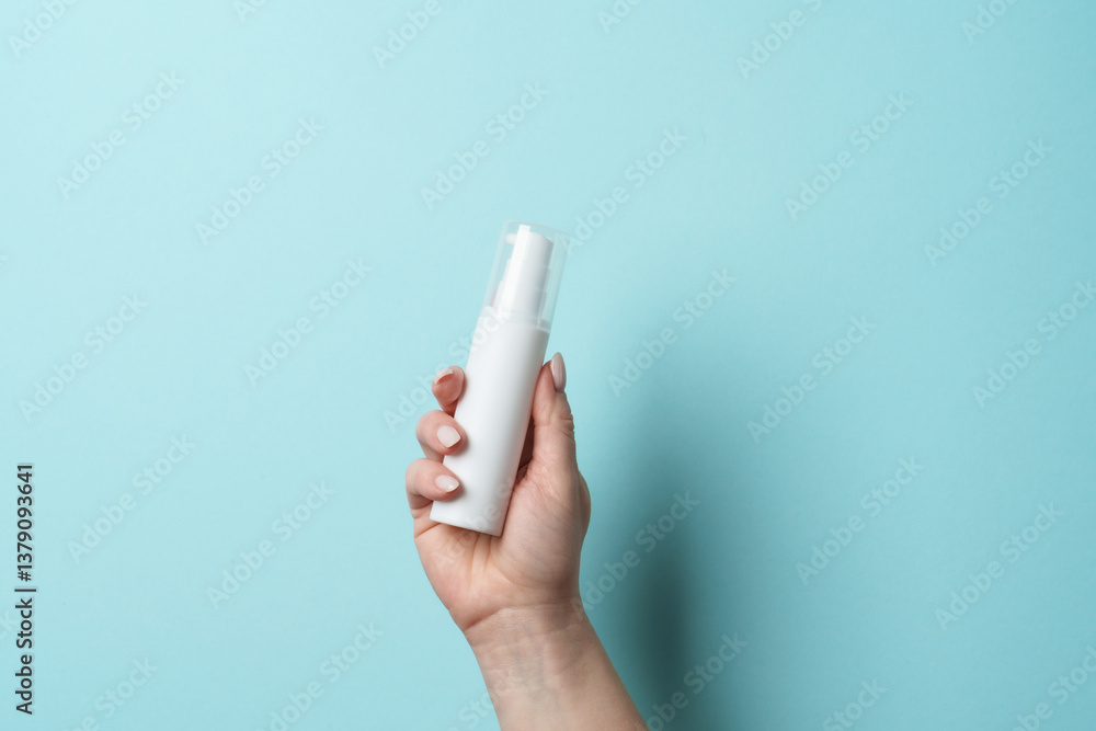 Cosmetic bottle in woman hand on blue background.