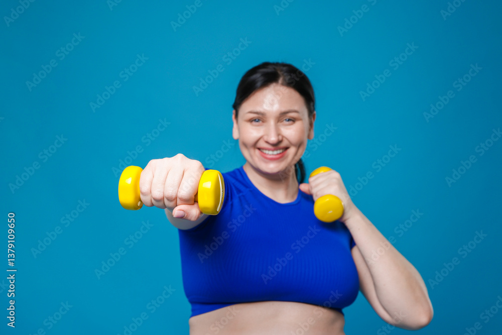 Plus size woman in gym clothes doing exercise with dumbbells on light blue background, selective focus Plus size woman in gym clothes doing exercise with dumbbells on light blue background, selective focus