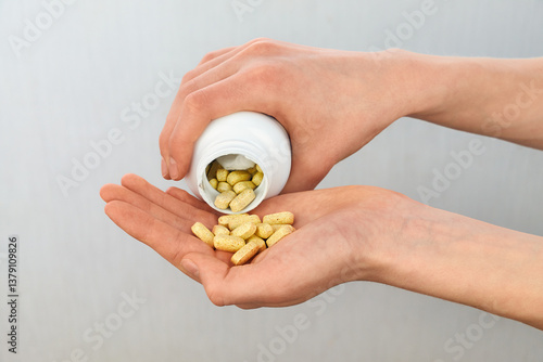 Hands pouring yellow vitamin pills from a white plastic bottle