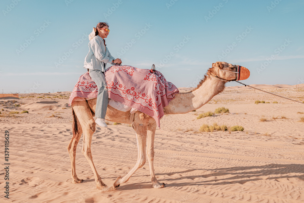 Smiling female tourist riding a dromedary camel in the desert during a sunny day
