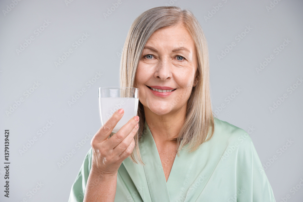 Smiling woman with glass of collagen water on grey background Smiling woman with glass of collagen water on grey background
