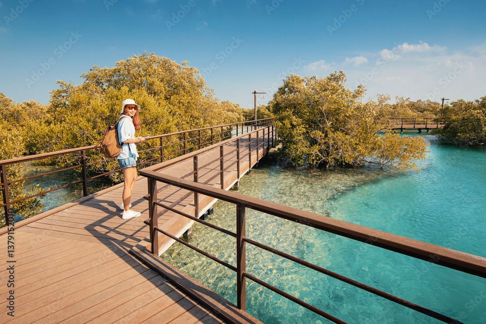 Female tourist with backpack walking on a wooden boardwalk enjoying the scenic mangroves in coastal park