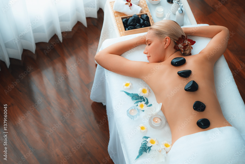 Fototapeta premium Panorama top view hot stone massage at spa salon in luxury resort with day light serenity ambient, blissful woman customer enjoying spa basalt stone massage glide over body. Quiescent