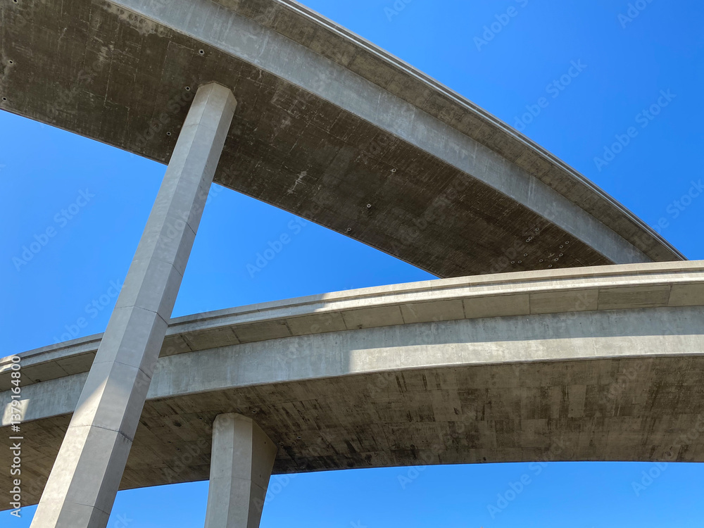 A view under two giant concrete freeway overpass bridges crossing paths under blue skies in San Diego California.