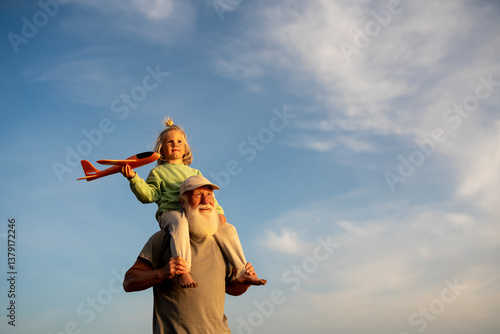 Fotografie Joyful little boy sitting on grandfather’s shoulders and holding a toy airplane