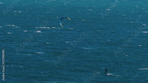 Distant view of a man kitesurfing on a sunny day