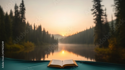 Fototapeta Naklejka Na Ścianę i Meble -  Morning light illuminates a serene lake with an open book resting on a green blanket