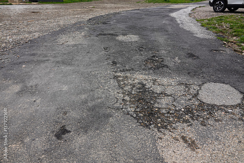 Obraz na płótnie A cracked and uneven road stretches through a suburban landscape, displaying various potholes and patches. w salonie