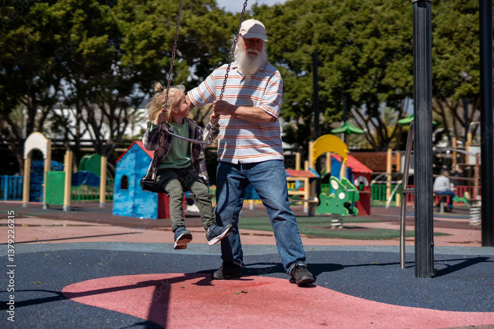 Obraz premium Loving grandfather in a striped shirt pushing his young grandchild on a swing at a colorful playground, sharing a joyful bonding moment on a sunny day