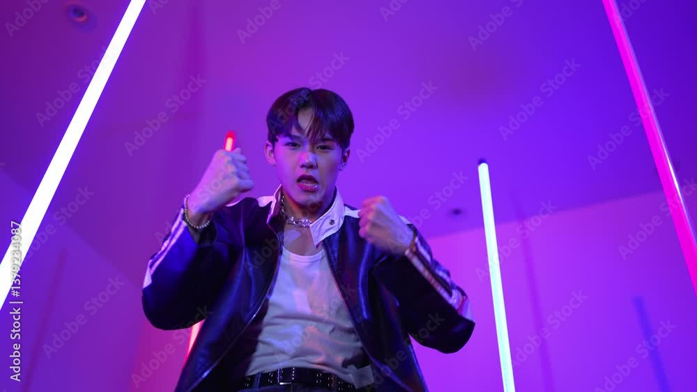 Low angle camera of professional street dancer looking at camera with casual cloth. Skilled performer moving to city pop music while standing at studio with purple led light. Close up. Regalement. Low angle camera of professional street dancer looking at camera with casual cloth. Skilled performer moving to city pop music while standing at studio with purple led light. Close up. Regalement.