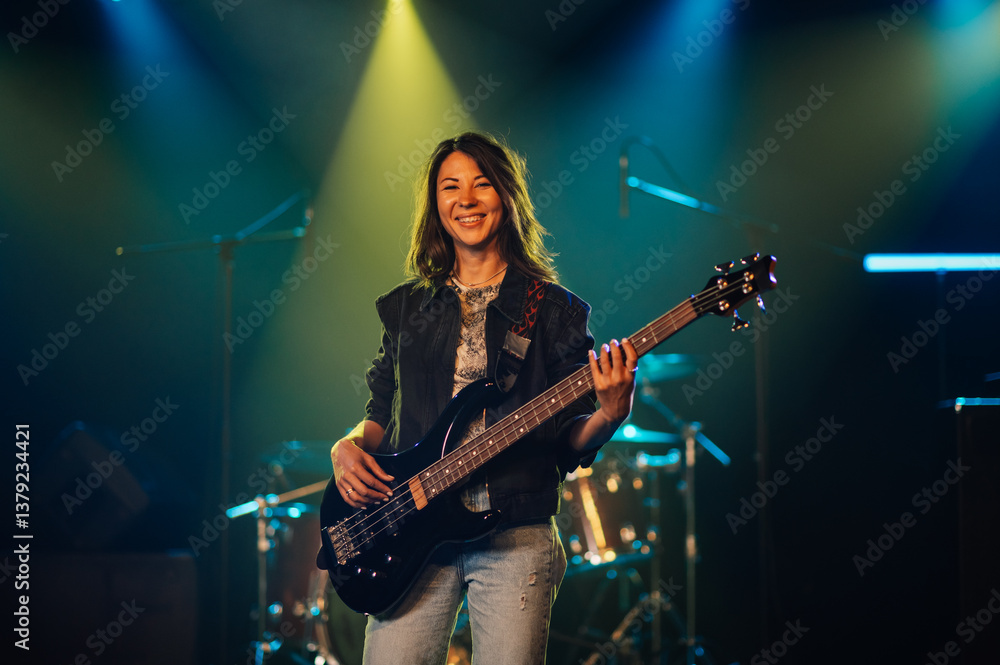 Fototapeta premium Female musician playing bass guitar on stage during concert