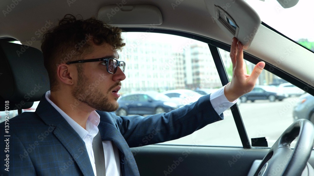 Young man sitting in his car on driver seat and looking at the mirror before the start of the trip. Transport, business and people concept. Slow motion Young man sitting in his car on driver seat and looking at the mirror before the start of the trip. Transport, business and people concept. Slow motion