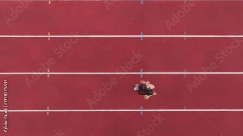 Top down view aerial drone shot of a professional female athlete sprinting on a large stadium athletics track. Dynamic slow motion cinematic footage captures her power, speed, and determination in