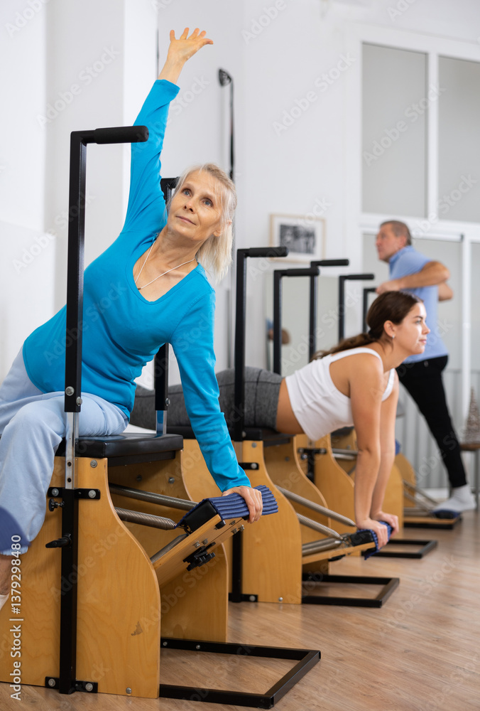 Calm senior woman performing stretching exercises while using pilates Wanda chair machine in rehabilitation center