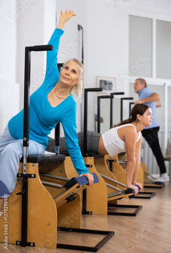 Obraz na płótnie Calm senior woman performing stretching exercises while using pilates Wanda chair machine in rehabilitation center w salonie