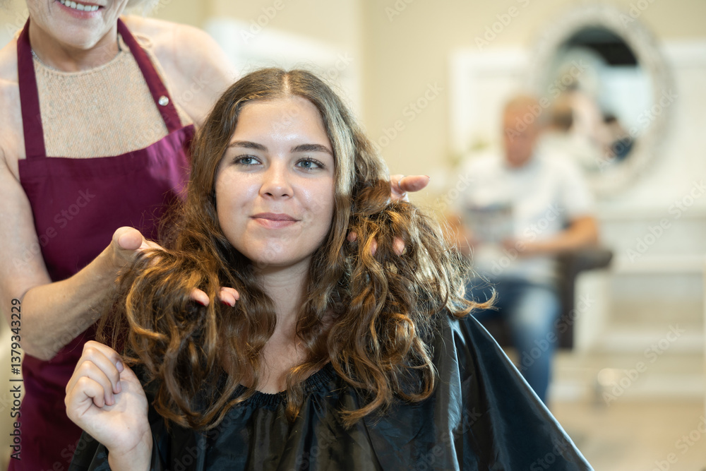 Naklejka premium Elderly professional hairdresser is doing fashionable haircut to young woman in hairdress salon