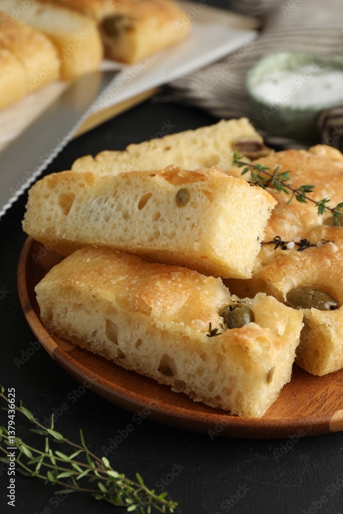 Slices of delicious focaccia bread with olives, thyme, salt and knife on black table, closeup Slices of delicious focaccia bread with olives, thyme, salt and knife on black table, closeup