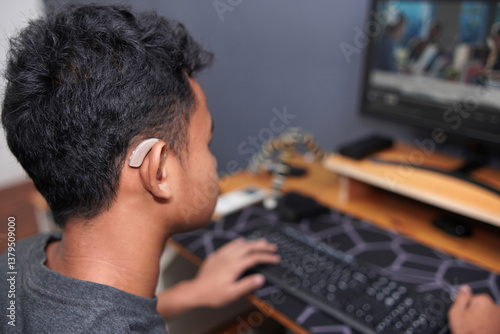 Asian boy with hearing aid device using computer