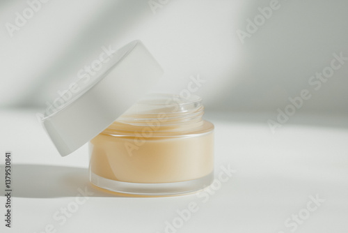 Obraz na płótnie Close-up of a jar of cream with a white lid on a white background, with shadows from a window. w salonie