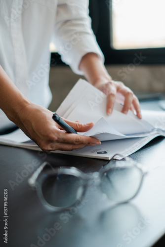 Close-up of hands organizing papers on a desk, with glasses and pen, in a modern office setting.