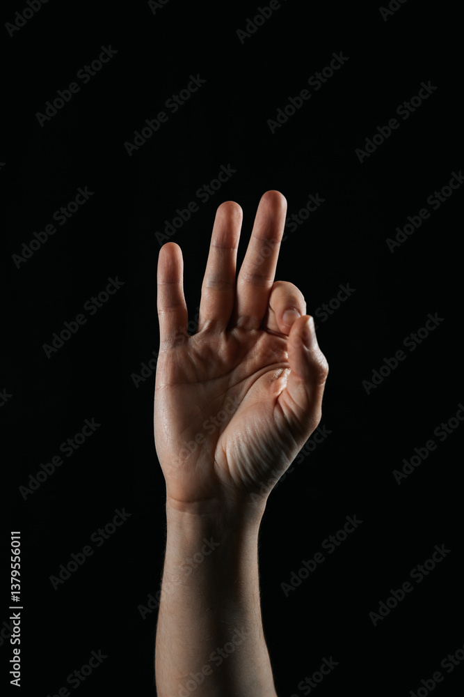 Close-up of a human hand showing three fingers up against a black background. Symbolic gesture used in communication, counting, or sign language. Close-up of a human hand showing three fingers up against a black background. Symbolic gesture used in communication, counting, or sign language.