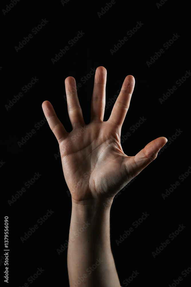 Close-up of an open human hand with spread fingers raised against a black background. Concept of stop, attention, number five, or communication. Close-up of an open human hand with spread fingers raised against a black background. Concept of stop, attention, number five, or communication.
