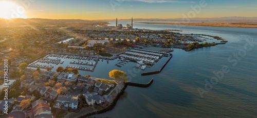 Aerial view of Pittsburg, California, USA, at sunset. The image shows the city's marina, waterfront homes, and a power plant in the distance. 
