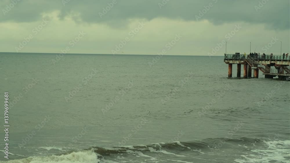 People Walking on a Pier Overlooking the Ocean at Dusk With Dramatic Clouds Above People Walking on a Pier Overlooking the Ocean at Dusk With Dramatic Clouds Above