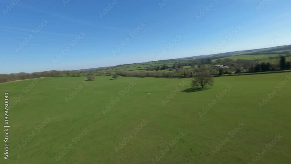 FPV aerial drone close proximity flying close across rural fields and around trees in England sunny day. FPV aerial drone close proximity flying close across rural fields and around trees in England sunny day.