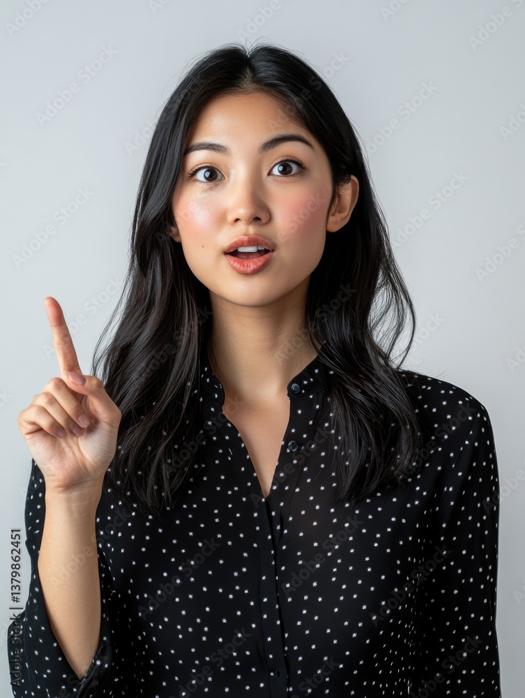 A woman with long black hair is pointing to the sky. She is wearing a black polka dot shirt