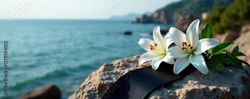 Black funeral ribbon and white lily flowers placed delicately on a weathered rock overlooking the tranquil sea,  mourning,  remembrance