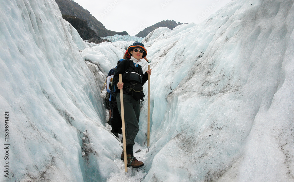 Woman walking on Franz Josef Glacier. People wearing ice crampons and walking on ice. South Island. New Zealand.