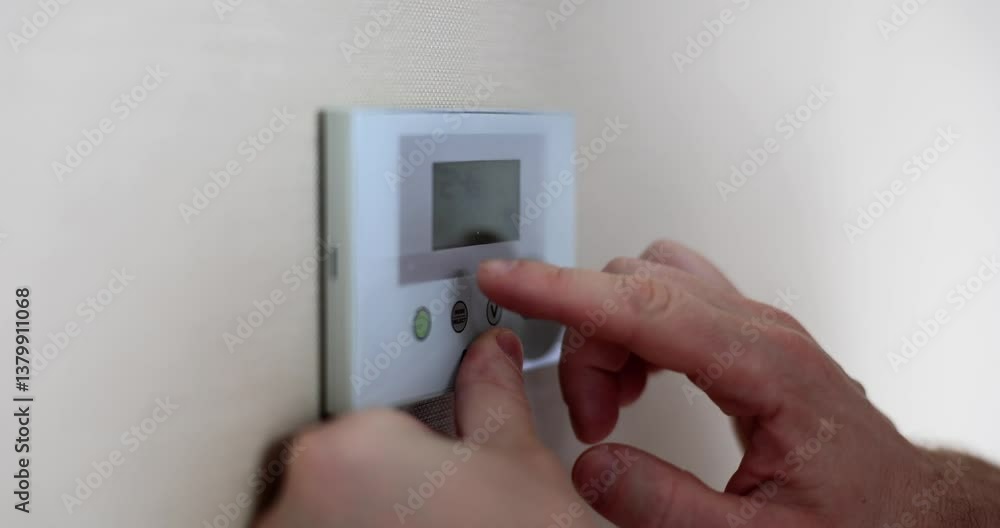 Man stands in hallway and presses buttons on security system panel. Guy selects correct settings to activate alarm. Male sets up alarm for night Man stands in hallway and presses buttons on security system panel. Guy selects correct settings to activate alarm. Male sets up alarm for night