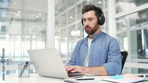 Wallpaper Mural Focused businessman or IT specialist in wireless headphones works on a laptop sitting at a workplace in a business office. Serious coder developer is programming, busy with a project on the computer Torontodigital.ca