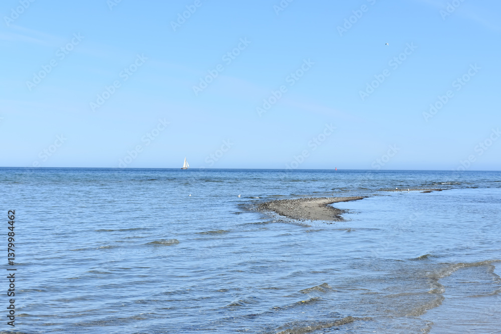 Fototapeta premium Sea and beach. White sailboat in the sea. Sea waves and sand. Travel. Sandy beach. Sea water. Horizon. Clouds in the sky.