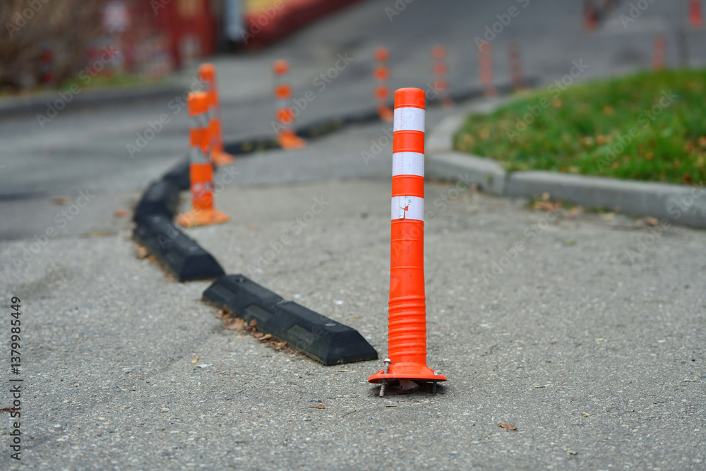 Damaged safety delineator with torn out fastening. Broken road infrastructure, plastic traffic cone. Orange traffic cones with reflective stripes guide vehicles along paved road. Selective focus