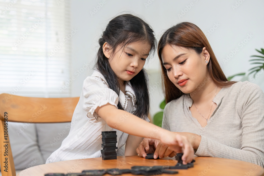 Connection and Playtime. A mother supporting her daughter as they play with dominoes together at the table. Connection and Playtime. A mother supporting her daughter as they play with dominoes together at the table.