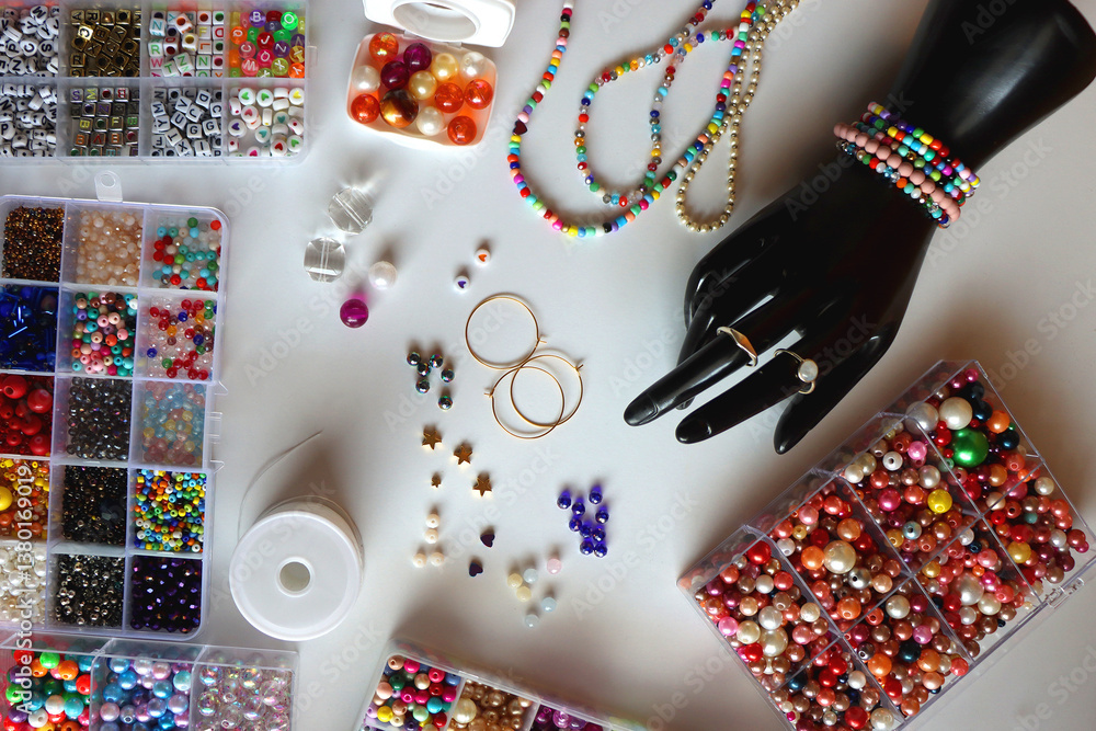 Hand figurine, colorful friendship bracelets, necklaces, various beads and DIY supplies on the table. Making jewelry at home. Flat lay.