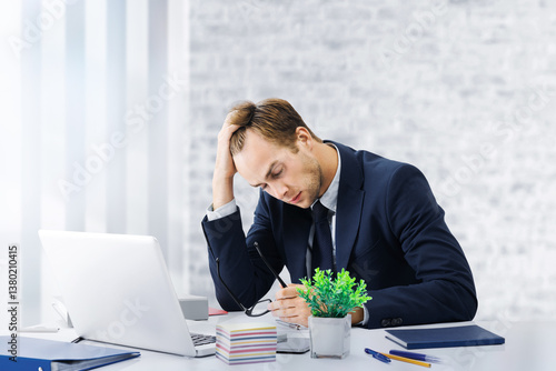 Stressed, tired businessman or having headache hold hand his head wear black suit jacket use laptop computer at office workplace desk. Portrait image - corporate pessimistic fall thinking business man