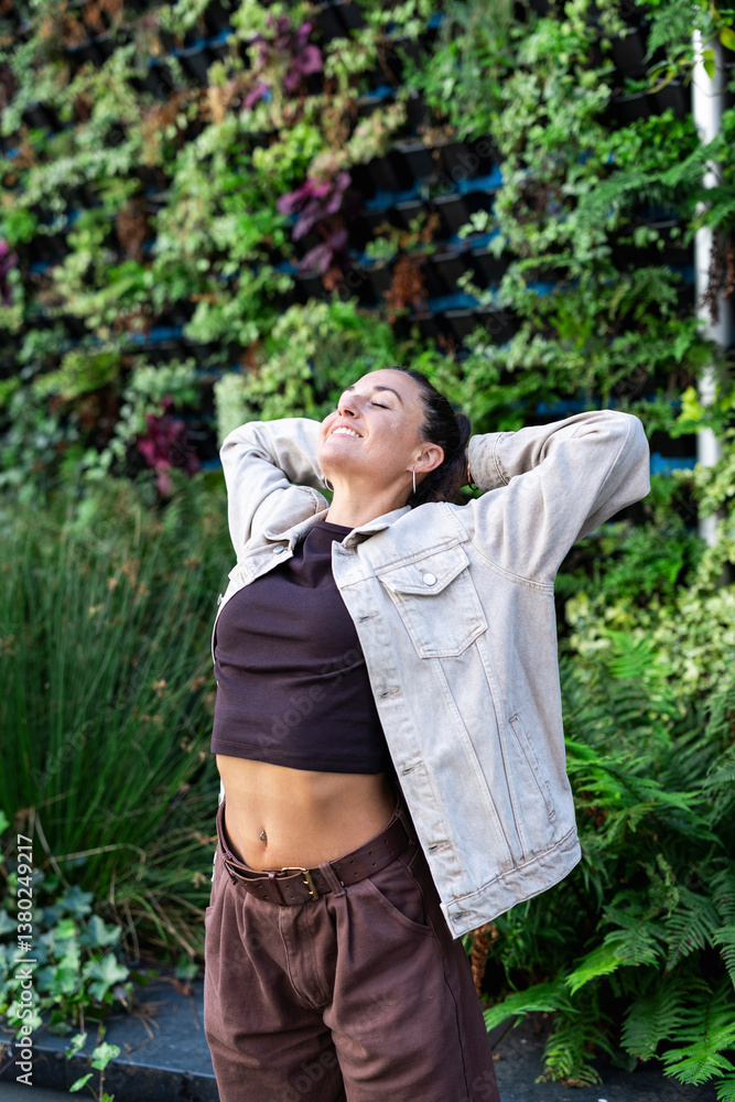 Happy woman enjoying a moment outdoors in the city with a vertical garden Happy woman enjoying a moment outdoors in the city with a vertical garden