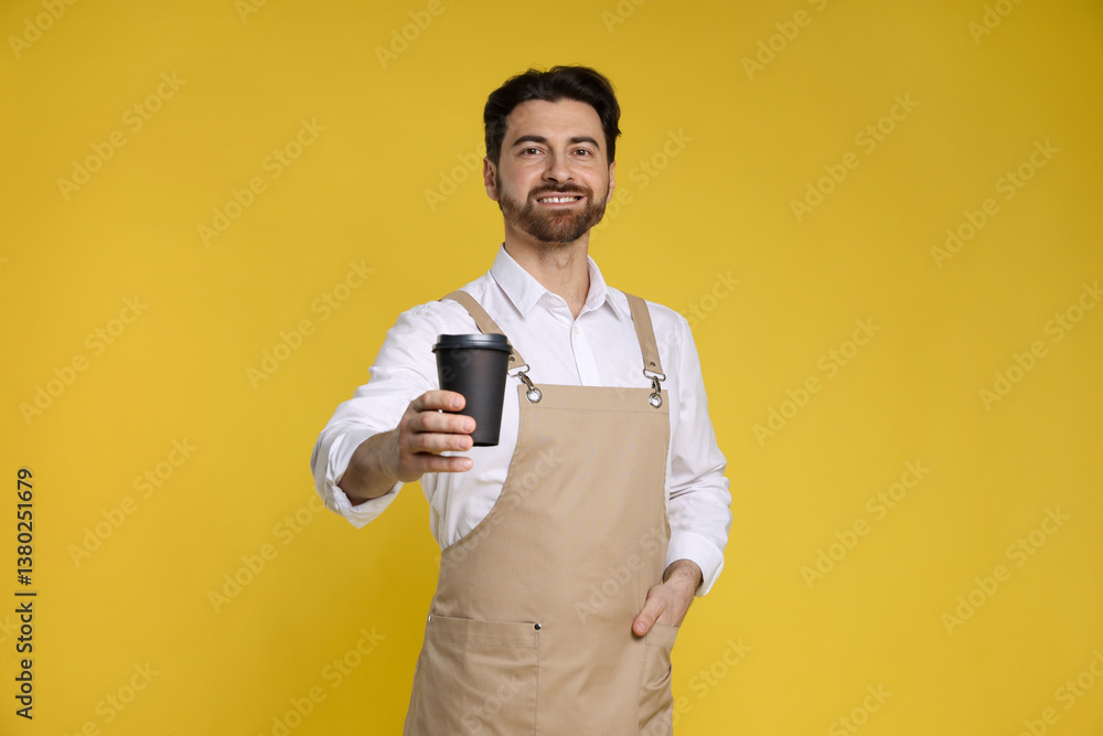 Portrait of smiling barista with paper takeaway cup of hot drink on yellow background Portrait of smiling barista with paper takeaway cup of hot drink on yellow background