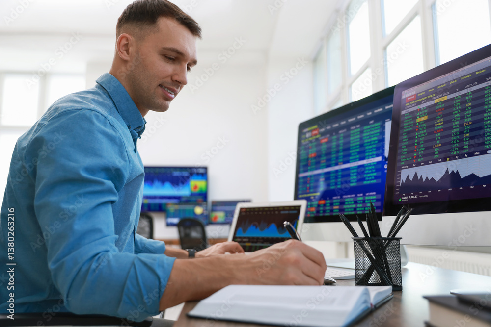 Financial trading specialist writing notes at table in office Financial trading specialist writing notes at table in office