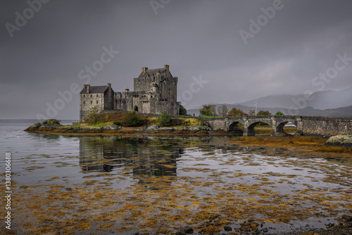 Obraz na płótnie Eilean Donan Castle stands majestically amid autumn hues, its reflection shimmering in calm waters. Misty Highlands and golden trees create a scene of timeless beauty. w salonie