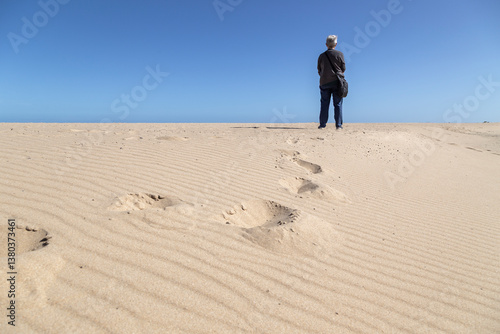 Принти на полотні Elderly person walking alone on sandy desert dunes under clear blue sky