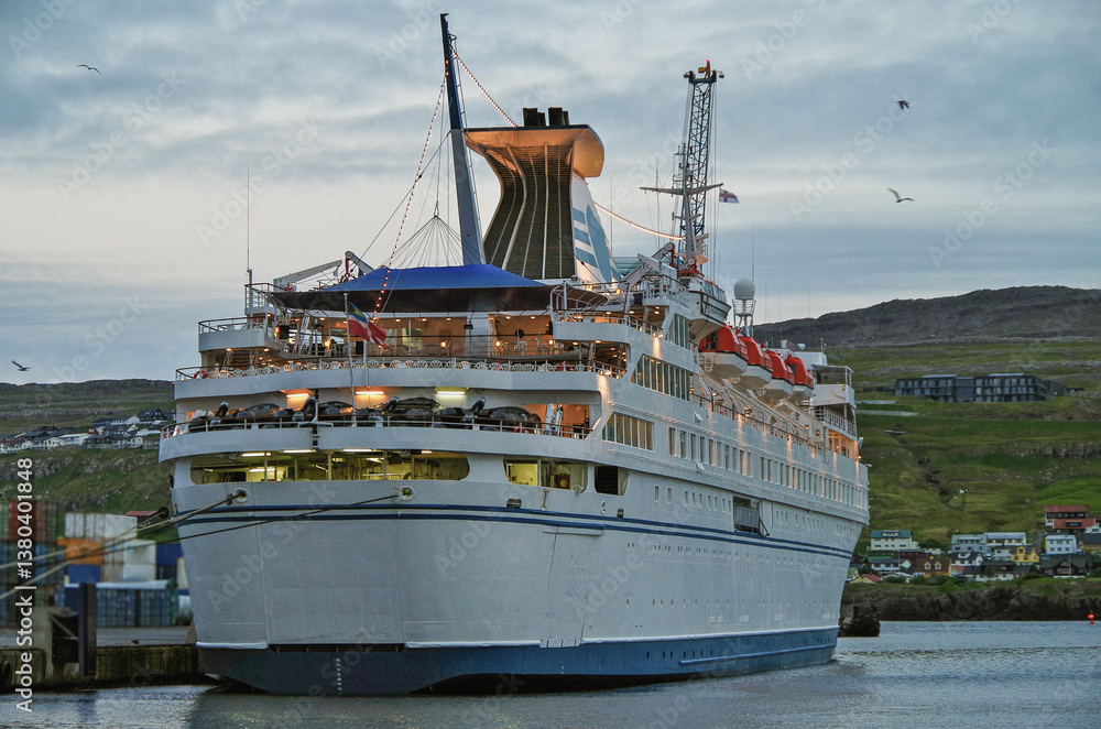 Classic expedition cruiseship cruise ship liner Delphin docked at pier in Thorshavn, Faroe Islands with cliffs and fjord landscape in background and city skyline during Arctic Circle summer cruising